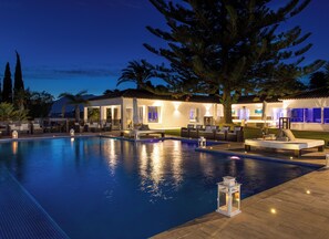 A swimming pool with lounge chairs and a sunbed, surrounded by palm trees and a building with outdoor lighting. - Luxury villa Issabella. (Marbella)