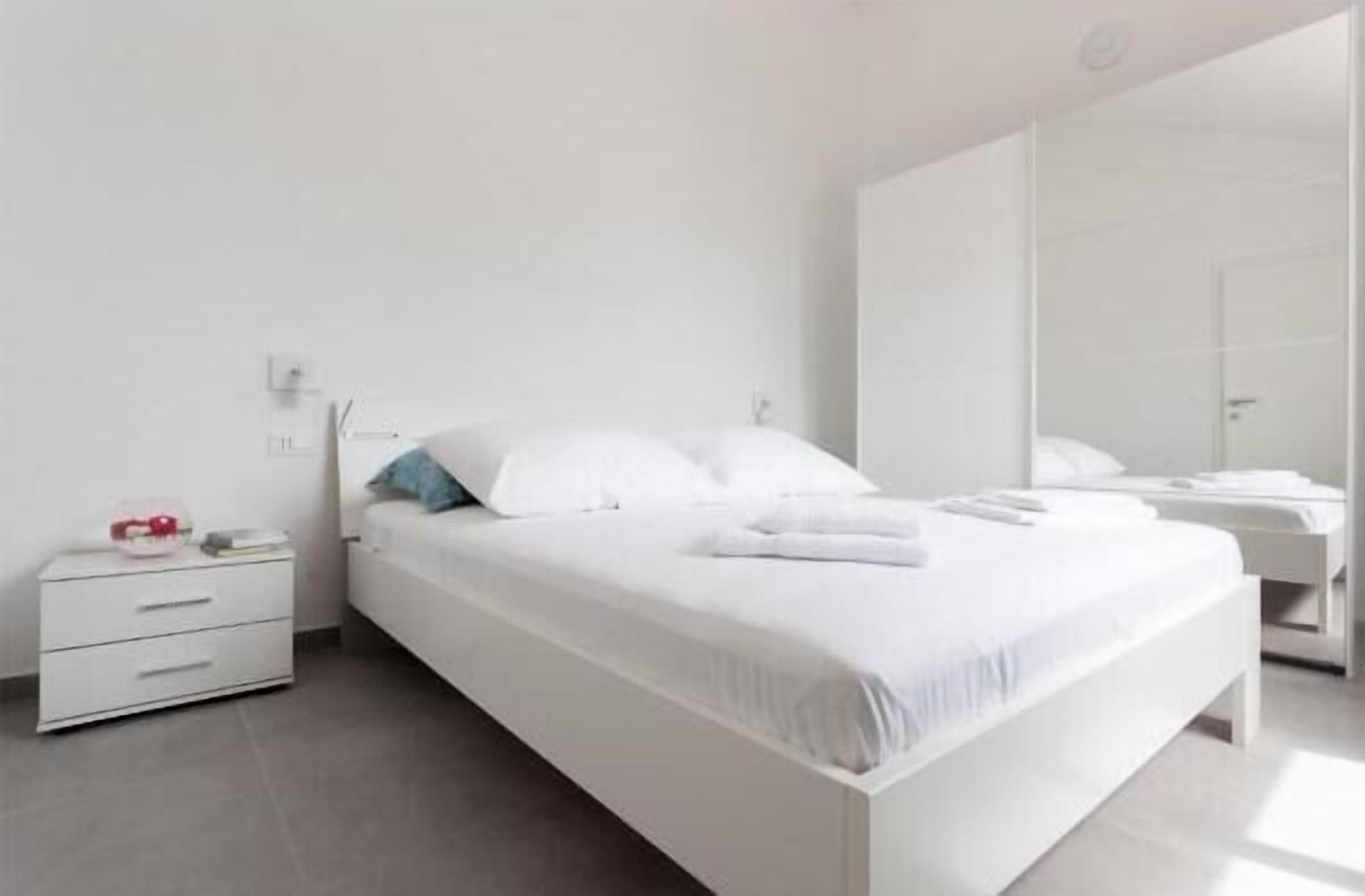 A modern bedroom with a large bed, a bedside table, and a wardrobe.