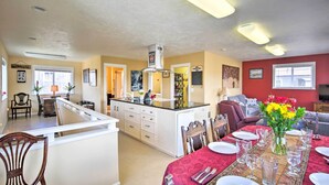 Amplia sala de estar con una mesa de comedor dispuesta para seis personas, una cocina con armarios blancos y una pared de acento roja.