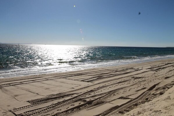 A sandy beach with tire tracks leading to the water.