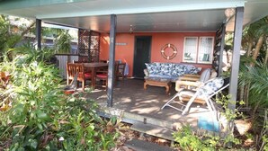 Ein überdachter Patio-Bereich mit Esstisch und Stühlen, einer Couch und einem kleinen Tisch mit Sessel.