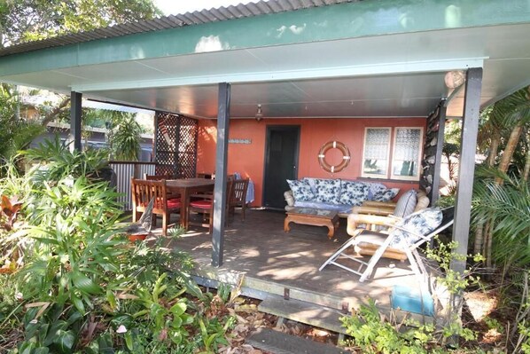 A covered patio area with a dining table and chairs, a sofa, and a small table with a chair. - Signal Cottage - Cowan Cowan - Moreton Island (Cowan Cowan)