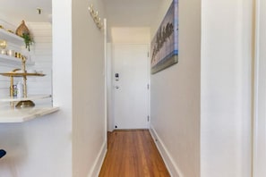 Un pasillo con piso de madera, paredes blancas, una puerta y un estante con adornos.