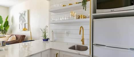 A modern kitchen with white cabinetry, a gold faucet, and a built-in microwave.
