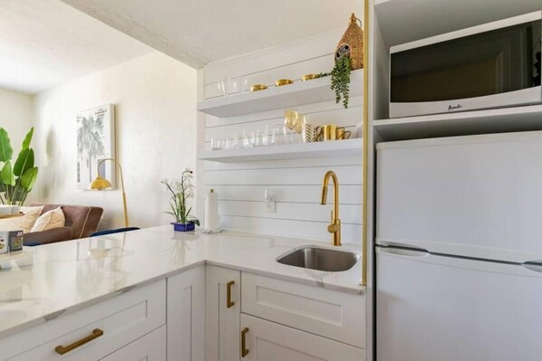 Una cocina moderna con armarios blancos, un grifo dorado y un microondas integrado.