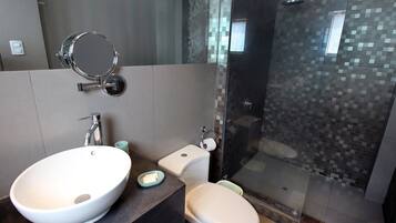 Un baño moderno con un lavabo blanco grande, un inodoro y una ducha con mampara de vidrio.