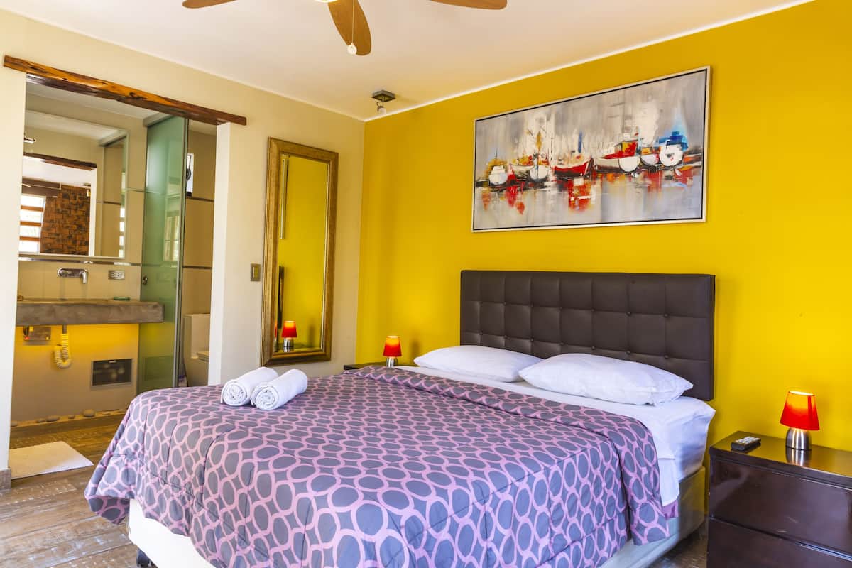 Una habitación de hotel con una cama, una mesita de noche, un espejo y un cuadro en la pared.