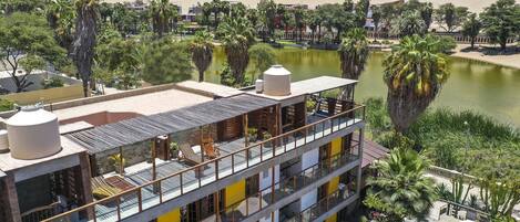 A multi-story hotel with balconies overlooking a lake, surrounded by palm trees and desert landscape.