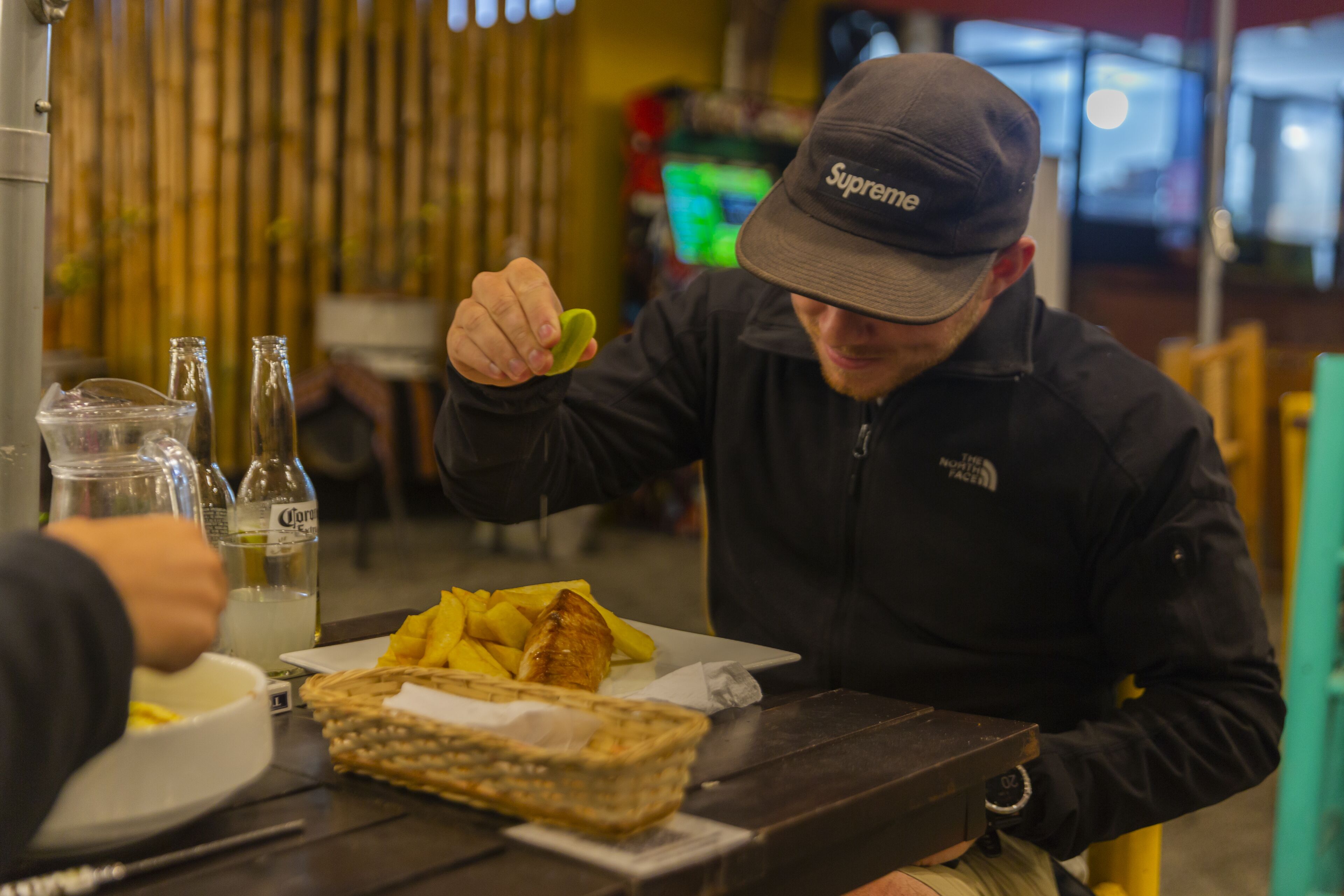 A person sitting at a table with a plate of food, a bottle of Corona beer, and a glass of water.
