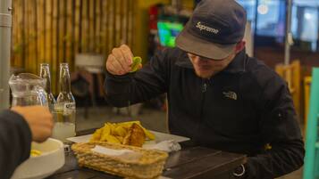 A person sitting at a table with a plate of food, a bottle of Corona beer, and a glass of water.