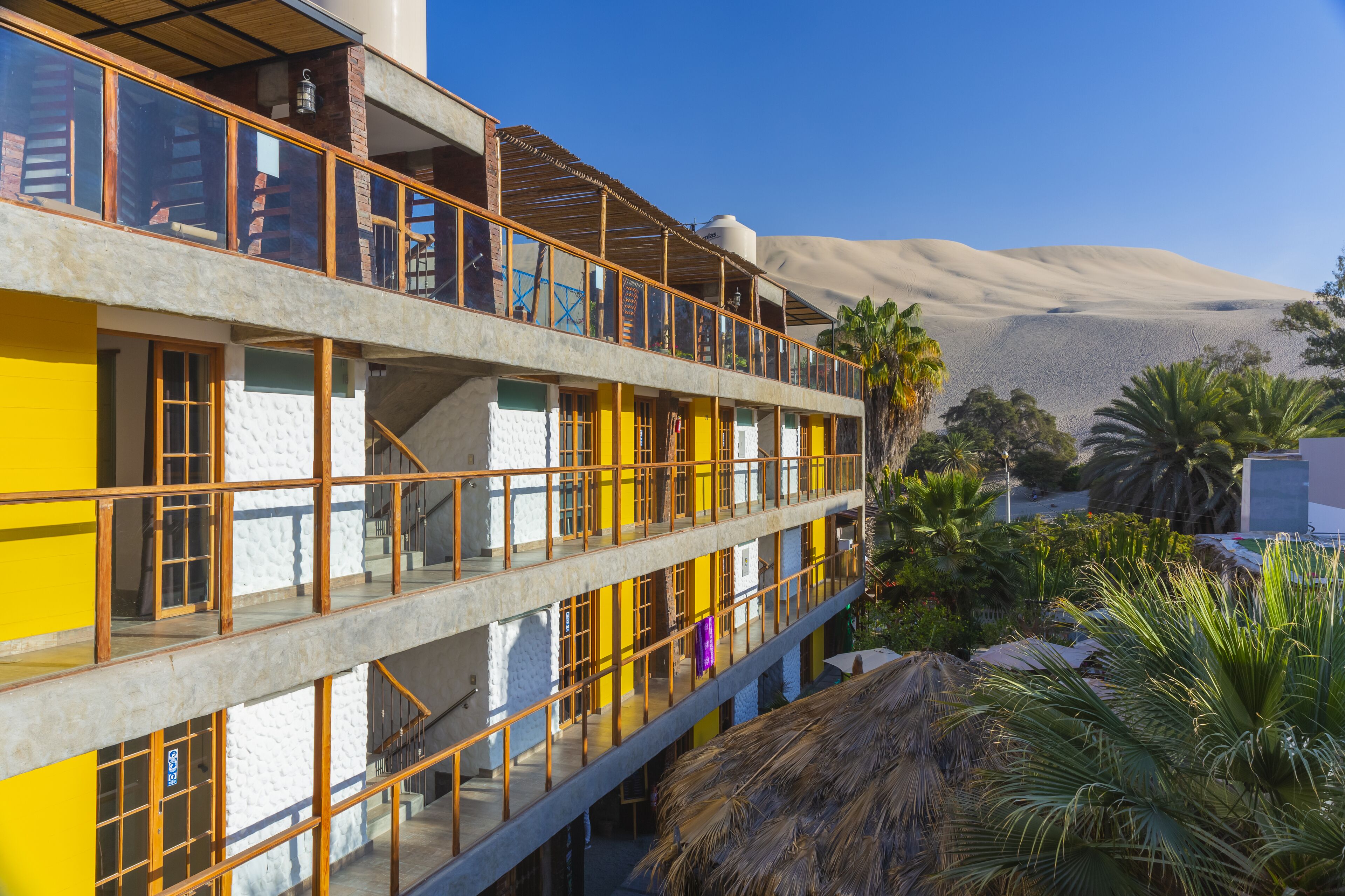 A multi-story building with balconies, a desert landscape in the background, and tropical plants in the foreground.