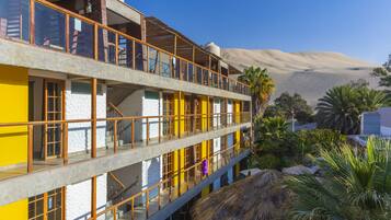 A multi-story building with balconies, a desert landscape in the background, and tropical plants in the foreground.