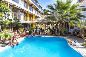 A pool area with a thatched-roof bar and lounge chairs. - Bananas Adventure Hostel (Ica)