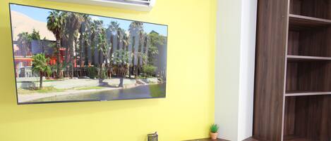 A room with a wooden desk, a chair, a television mounted on the wall, and a small potted plant.