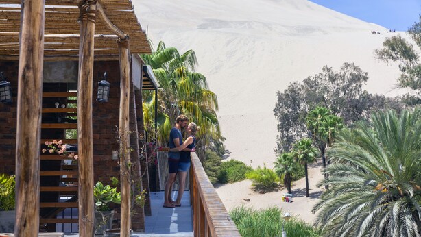 A wooden deck with a railing overlooking a sandy beach and palm trees. - Bananas Adventure Hostel (Ica)