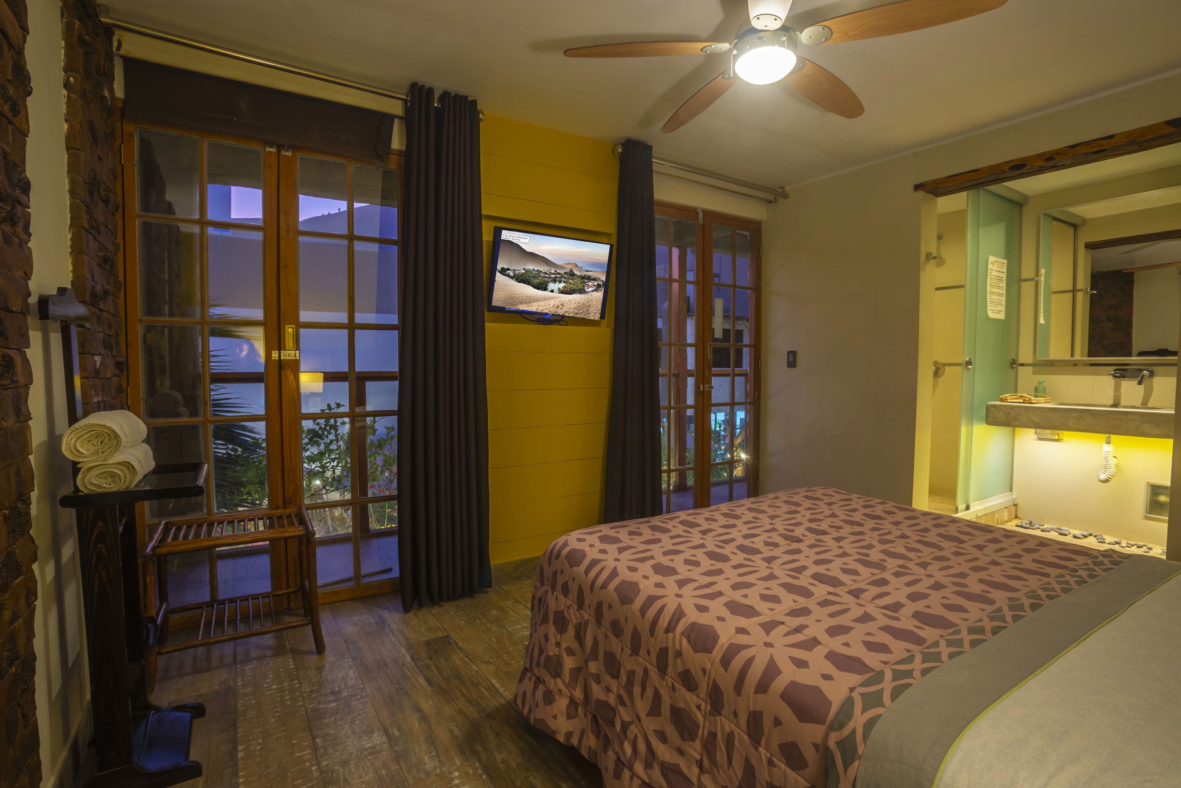 A bedroom with a bed, a television, a ceiling fan, and a window with curtains.