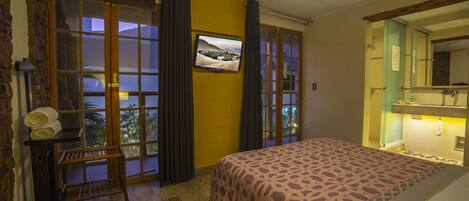 A bedroom with a bed, a television, a ceiling fan, and a window with curtains.