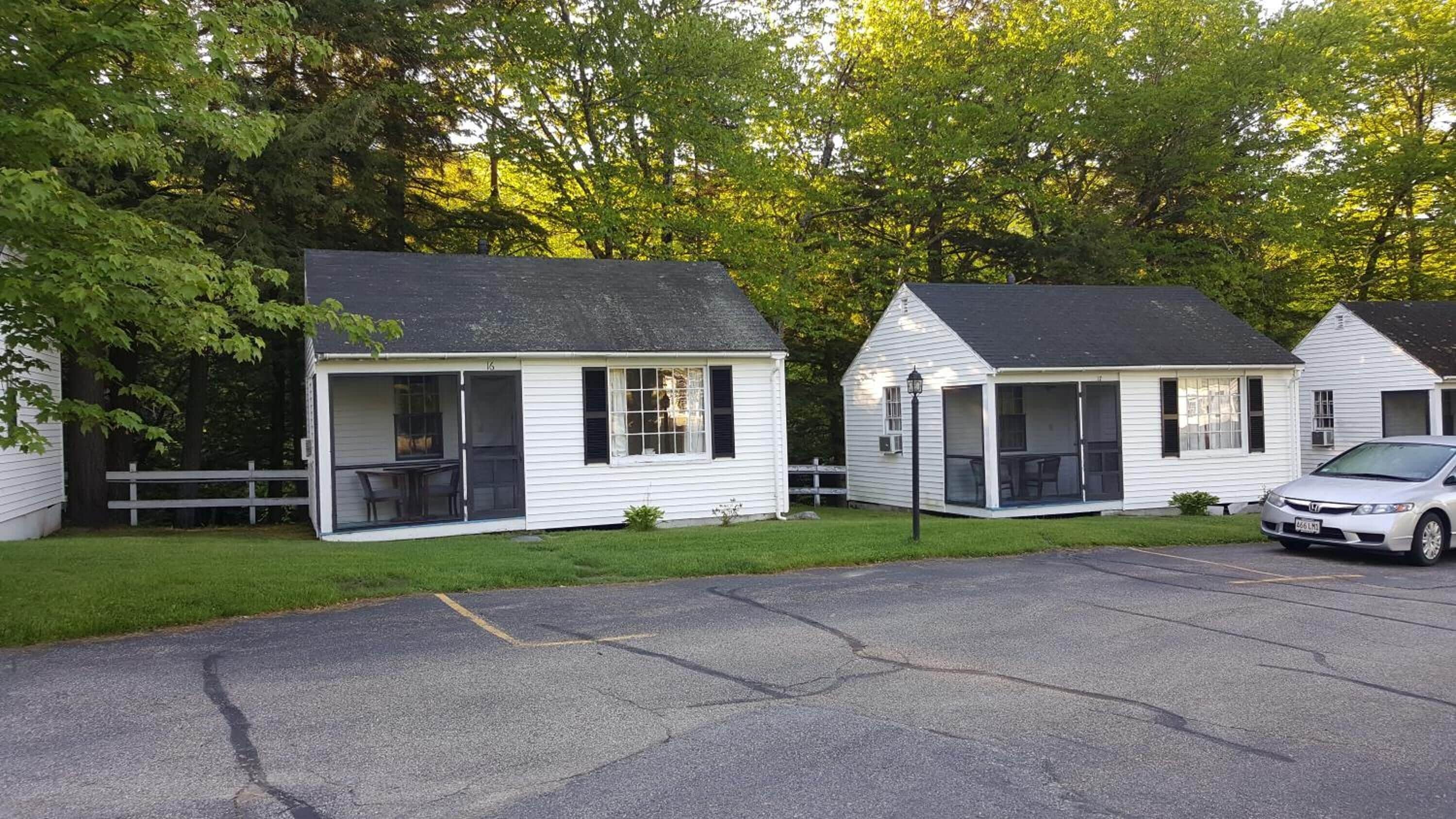 A row of small, white cabins with attached porches, surrounded by trees.
