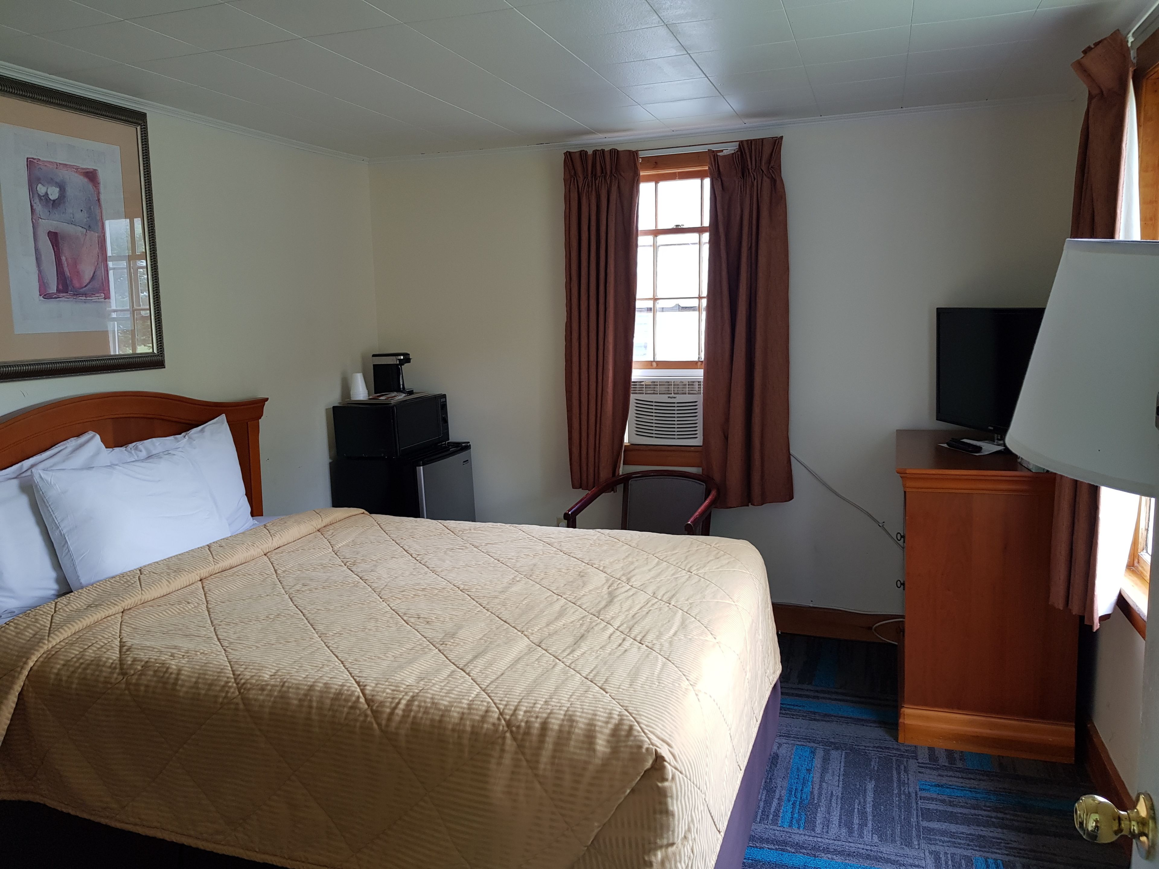 A hotel room with a bed, a desk with a computer, a television, and an air conditioning unit.