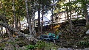 A rustic cabin with a wooden deck and a picnic table in a forested area. - Franconia Notch Motel (Lincoln)