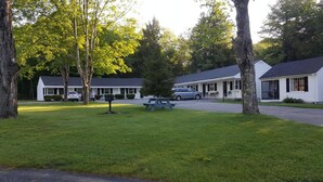 A motel with a grassy front yard, picnic table, and several cars parked in front. - Franconia Notch Motel (Lincoln)