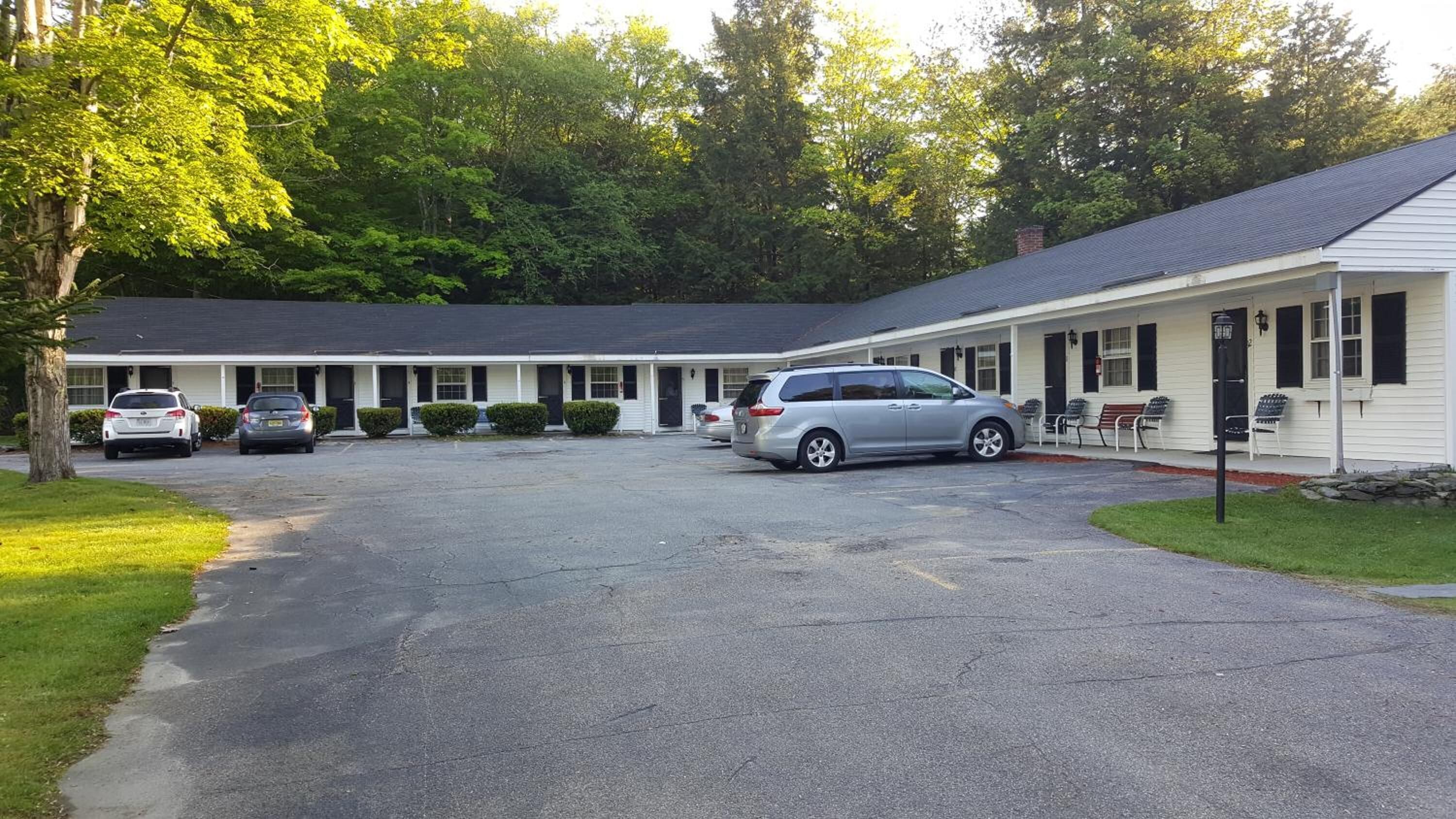 A motel with a central parking area, a covered walkway, and a row of rooms with a single-story structure.