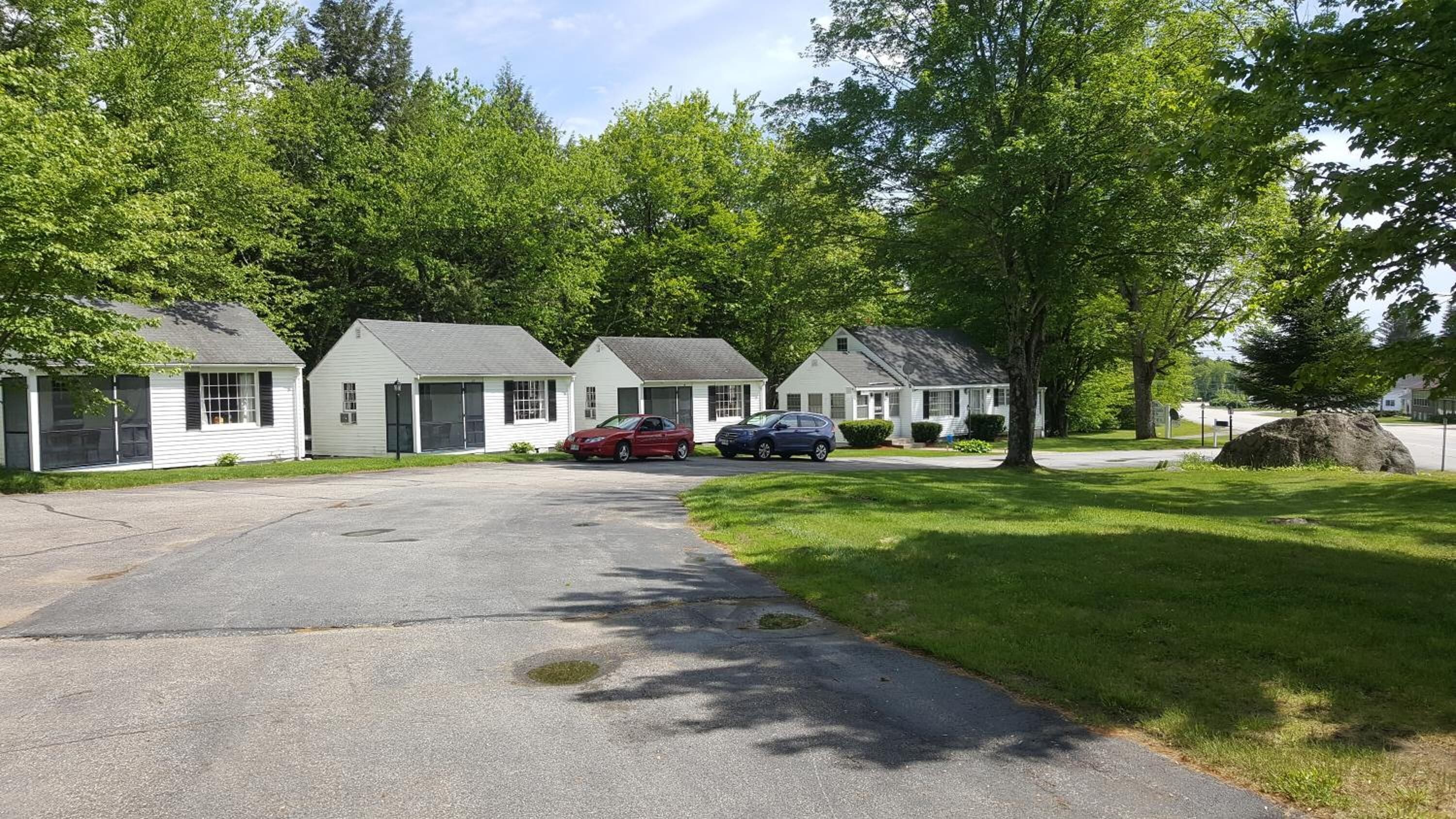 A row of single-story houses with attached garages, a paved driveway, and a large rock in the foreground.