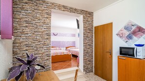 Quarto compacto com parede de pedra, cama com roupa de cama listrada, micro-ondas e uma pequena mesa com um vaso.