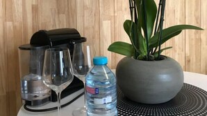 Une table avec une bouteille d’eau, un verre et une machine à café. On y voit également une orchidée en pot et un panneau indiquant « bonjour ».