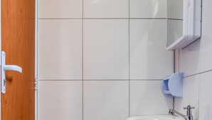 A bathroom with white tiles, a wooden door, a sink, a mirror, and a toilet. - HOTEL PAULISTANO Center Norte (São Paulo)