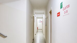 A narrow, well-lit hallway with a tiled floor, leading to a door at the end. There are signs on the wall indicating room numbers and a fire extinguisher mounted on the wall. - HOTEL PAULISTANO Center Norte (São Paulo)