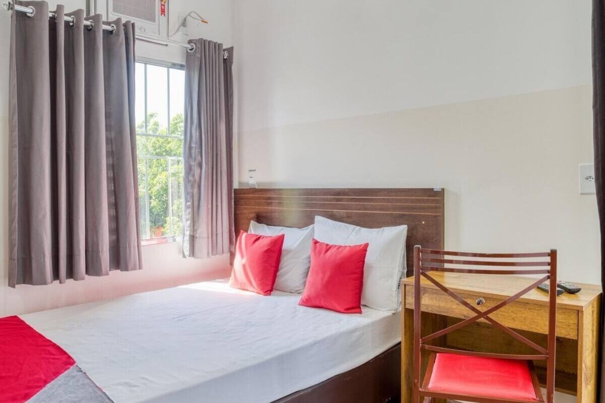 Una cama individual con cabecera de madera, cortinas grises y un escritorio de madera con una silla.