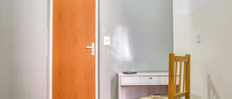 Une pièce avec une porte en bois, un bureau avec une chaise et deux lits avec une literie rouge et blanche.