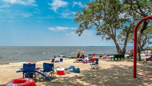 A beach with blue chairs, a red inflatable ring, and a tree providing shade. - Sound Waves - Colington Harbor, Waterfront, Pets OK, Community Pool & Soundfront Beach (Kill Devil Hills)