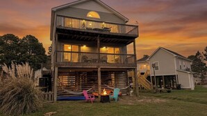 A two-story house with a balcony, a fire pit, and outdoor seating. - Sound Waves - Colington Harbor, Waterfront, Pets OK, Community Pool & Soundfront Beach (Kill Devil Hills)