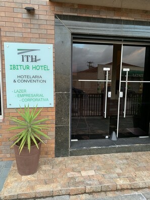 Placa do Hotel Ibitur, indicando que oferece serviços de hotelaria, convenções e corporativos, incluindo uma cafeteria.
