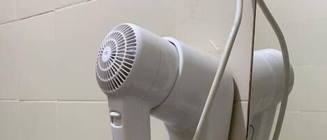Un secador de pelo sujeto a una pared de azulejos, conectado a un cable enrollado.