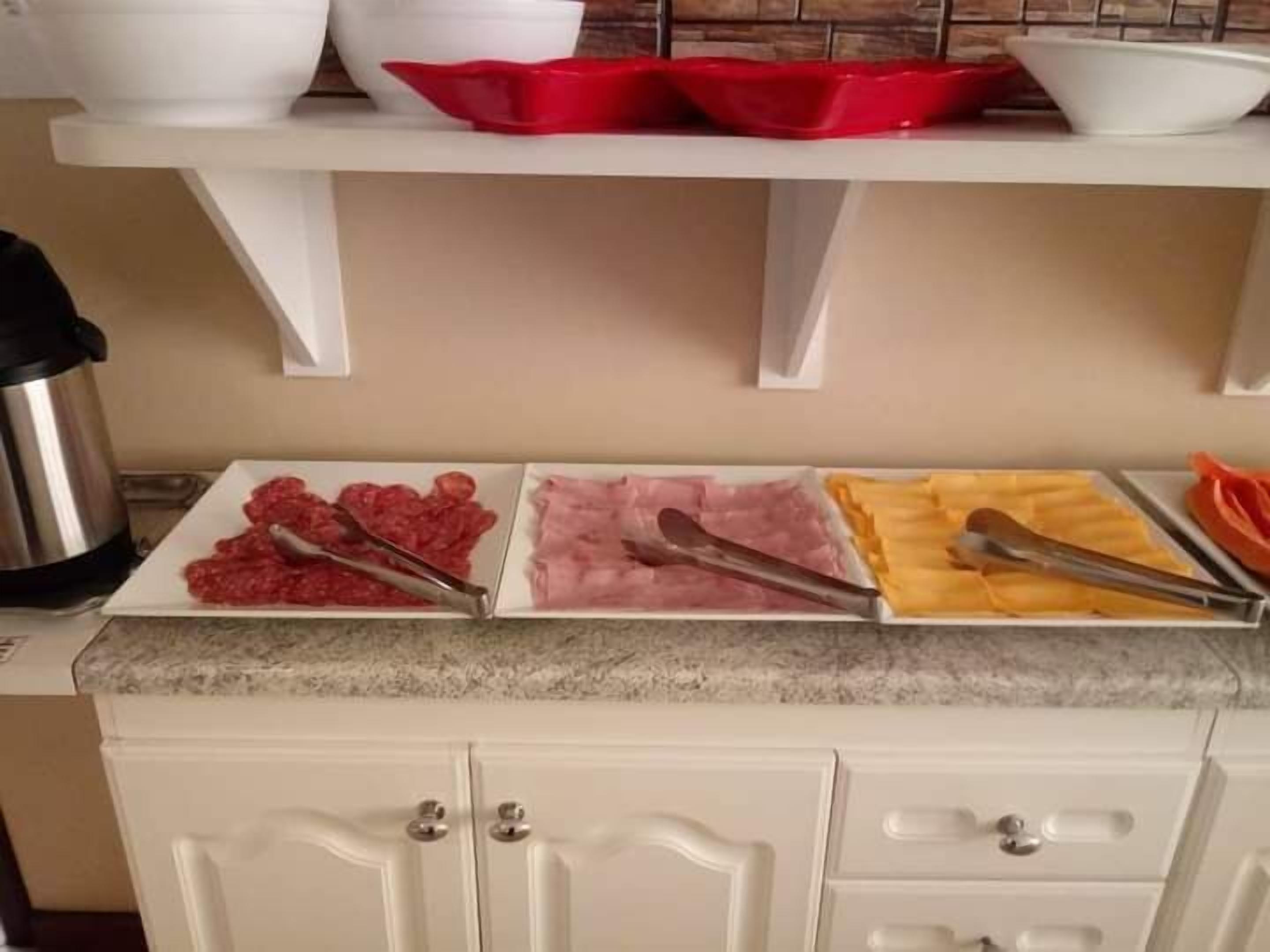 A kitchen counter with three trays of food, a kettle, and white cabinets.