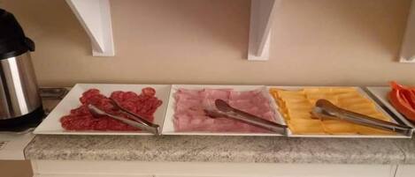 A kitchen counter with three trays of food, a kettle, and white cabinets.