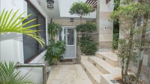 Un edificio moderno con una escalera que lleva a una puerta, rodeado de plantas en macetas y un pequeño árbol.