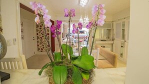 Una habitación con una orquídea grande en maceta sobre una mesa de mármol, una silla blanca y una araña.