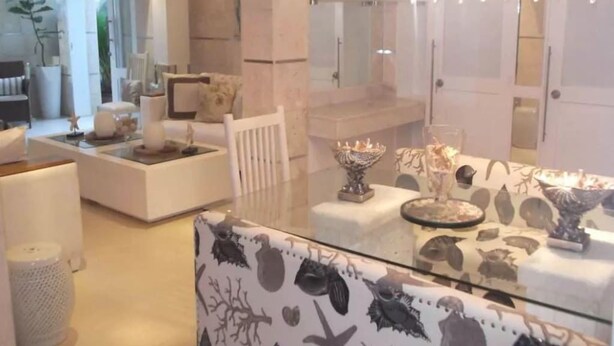 Una habitación de hotel moderna con una mesa de comedor de vidrio, muebles blancos y una araña.