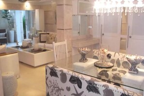A modern hotel room with a glass dining table, white furniture, and a chandelier. - 2BR Altos Chavon Apartment by ASVR-C1A (La Romana)