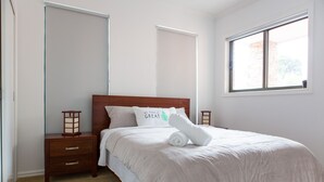 A neatly made bed with a white comforter and a pillow with a green leaf design. - 5 Bedroom | 3 Bathroom Holiday Home near Glen Waverley with WIFI and NETFLIX (Forest Hill)