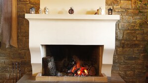 A stone fireplace with a white mantel, lit fire, and hanging lights. - Hotel Athina (Zagori)