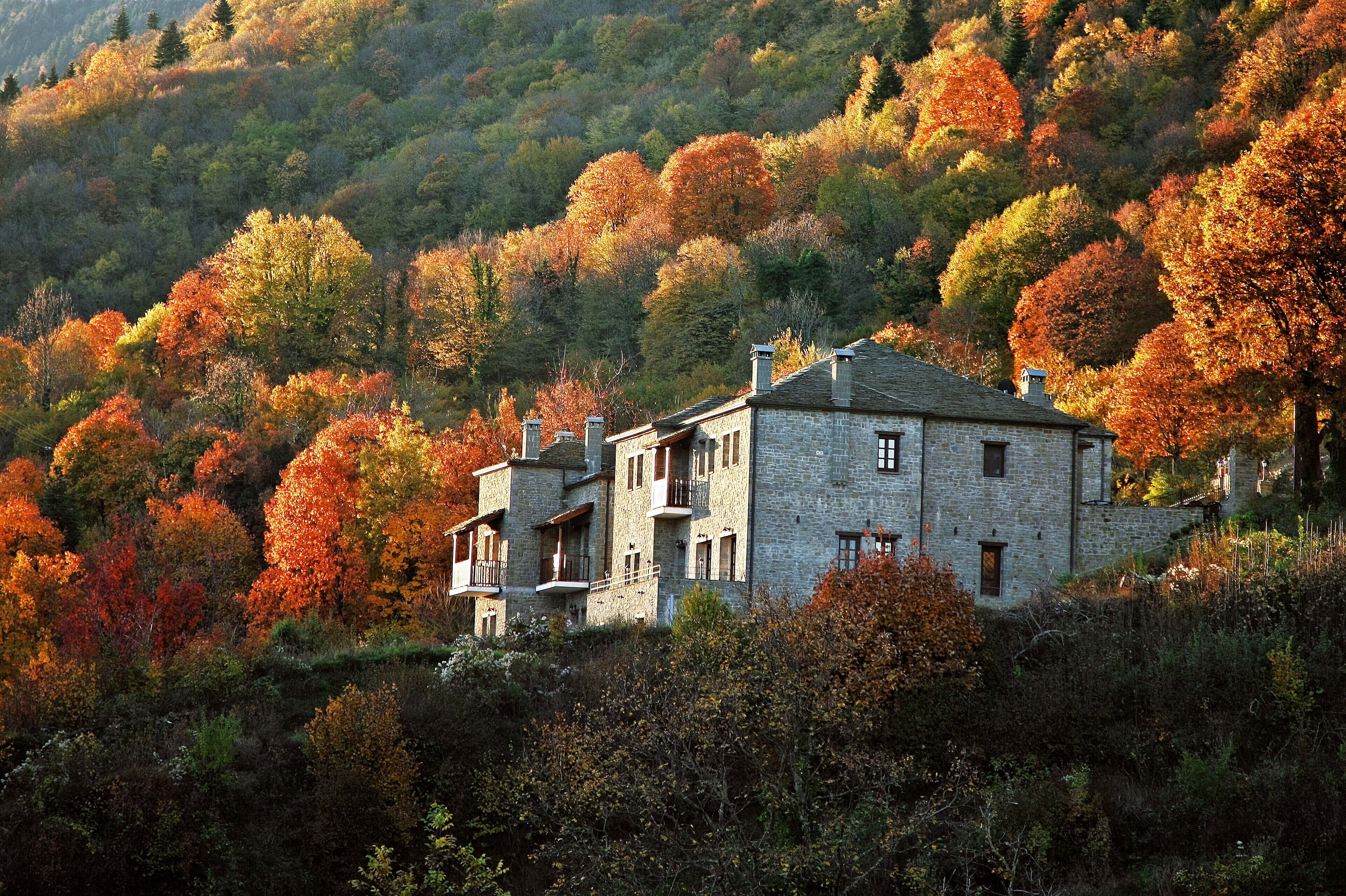 A stone building with multiple balconies, surrounded by autumn foliage on a hillside.