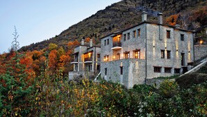A stone building with multiple balconies and windows, surrounded by autumn foliage and a hillside. - Hotel Athina (Zagori)