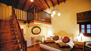 A bedroom with a wooden staircase, a bed with floral bedding, a desk, and a chair. - Hotel Athina (Zagori)