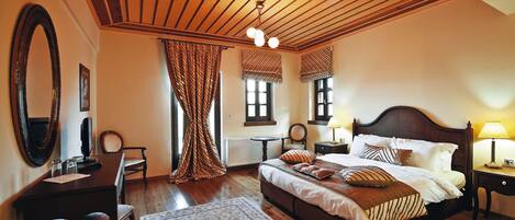 A bedroom with a large bed, a desk, a chair, a mirror, and a window with curtains.
