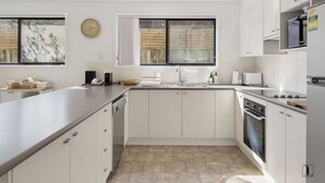 A modern kitchen with white cabinetry, a large island, a built-in oven, and a window with curtains. - Seaside Living, Steps to the Beach (LONG BEACH)